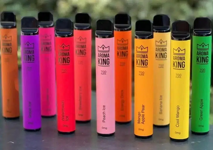 Zbiór kolorowych e-papierosów jednorazowych, takich jak Aroma King i Crystal, atrakcyjnie ułożonych na półce sklepowej, symbolizujących ich popularność.