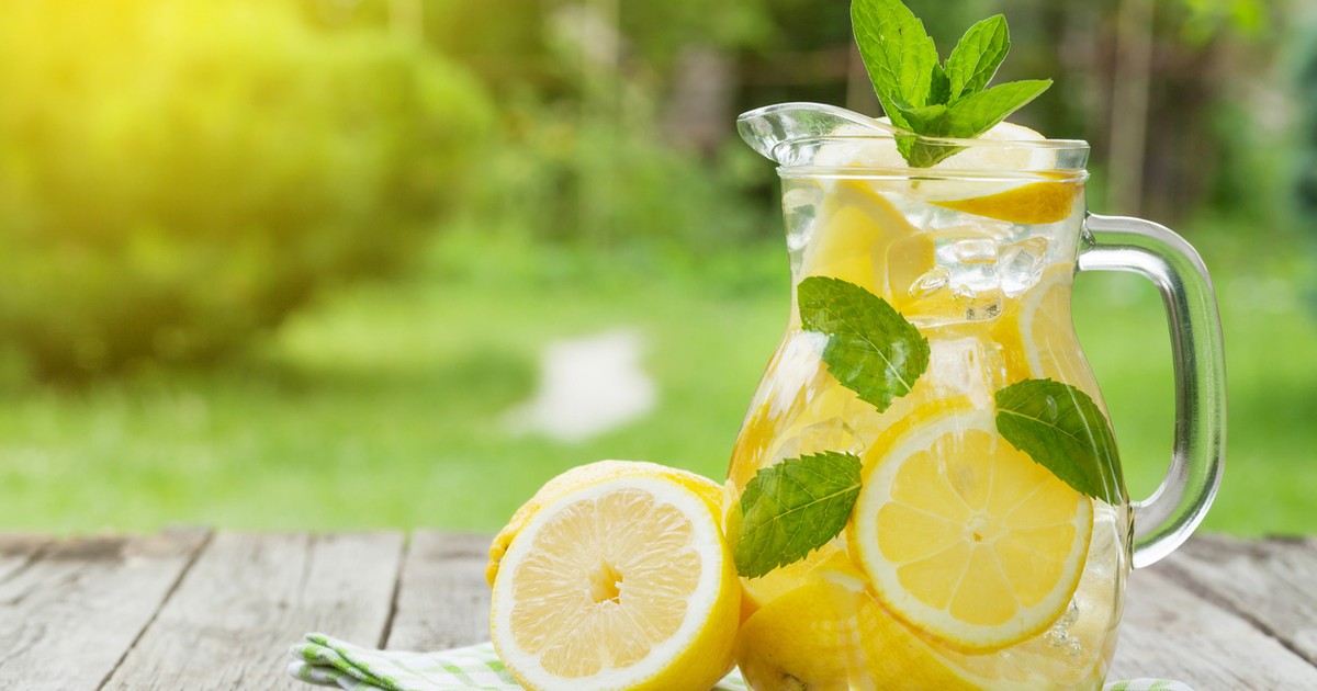 Szklanka zimnej, domowej lemoniady z plasterkami cytryny, listkami mięty i kostkami lodu, stojąca na stole w upalny dzień.