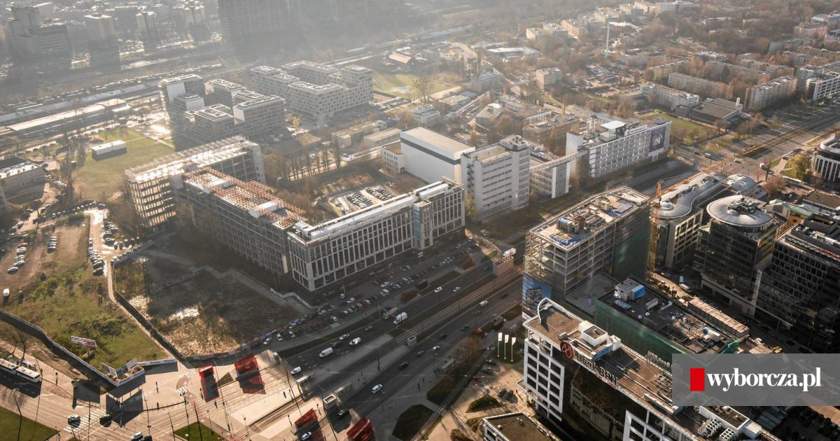 Osoba stojąca w deszczu przed nowoczesnym biurowcem w Warszawie na Rondzie Daszyńskiego, po szybkim paleniu papierosa, z wyrazem dyskomfortu związanego z zapachem dymu.